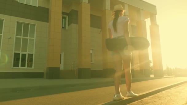 Menina adolescente livre ir com um skate em suas mãos na rua na cidade. skatista feliz viaja na estrada ao ar livre no parque. estilo de vida de um adolescente moderno. — Vídeo de Stock