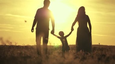 Bebekli mutlu bir aile güneşte tarlada yürüyor. Anne, baba ve bebek dışarıda oynuyorlar. Sağlıklı küçük kız gün batımında anne ve babasının kollarında atlar ve uçar. çocuk aile kavramı.