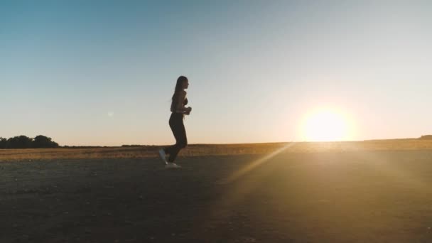 Вільна молода жінка біжить в літньому парку на заході сонця. біжить після сонця. тренування бігу. Здорова красива дівчина займається фітнесом, бігом по країні на сонці. Дівчина Джоггер дихає свіжим повітрям на полі . — стокове відео