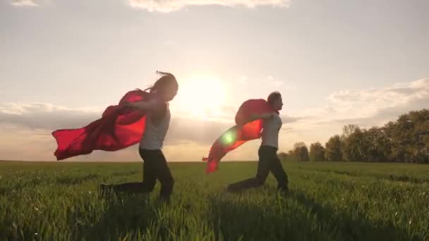 Tieners dromen ervan om superheld te worden. Jonge meisjes met een rode mantel. gelukkige meisjes spelen superhelden ze lopen over het groene veld in rode mantel, camouflage fladders in de wind. spelletjes en dromen van kinderen. Langzame beweging. — Stockvideo
