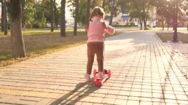 Sağlıklı bir çocuk sokakta scooter kullanıyor. Mutlu çocukluk kavramı. Küçük kız scooter sürmeyi öğreniyor. Parkta oynayan mutlu kız bebek.