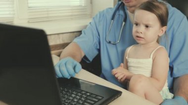 Çocukları tedavi etmek için pediatrik muayene kavramı. Profesyonel erkek doktor çocuk doktoru, tatlı anaokulu çocuğuyla oynayan ve dizüstü bilgisayarda çalışan. Hasta kız çocuk doktorunun kucağına oturuyor.