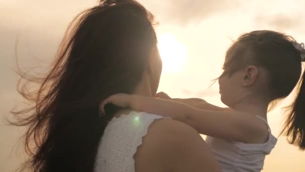 Mom and cute baby hug in sun. Happy family mom and daughter in the field at sunset. Mom and daughter stretch out their hands to sun, playing with rays. Happy family and healthy childhood concept — Stock Video