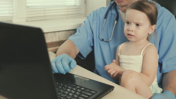 Gyermekgyógyászati vizsgálati koncepció a gyermekek kezelésére. Gondoskodó professzionális férfi orvos gyermekorvos, játszik aranyos óvodás gyermek és dolgozik laptop. lány beteg ül az ölében a gyermekorvos — Stock videók
