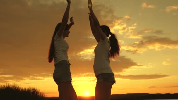 Özgür kızlar bir yaz akşamı gün batımında neşeyle dans ederler. Açık hava kutlaması. Yaz gününü bir plaj partisiyle kutlarız. Sağlıklı gençler sevinçle ellerini kaldırır. Sahilde eğlenceli tatil — Stok video