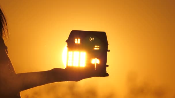 Hand silhouette with a toy house in rays of warm sun, rays of flash through windows and doors. in palms of the child dream of his home. family beautiful home concept. beautiful real estate at sunrise. — Stock Video