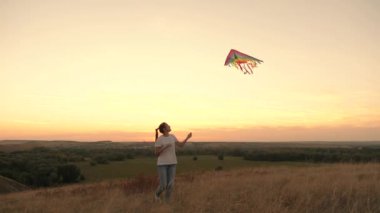 Genç kız gökyüzüne çok renkli bir uçurtma fırlatıyor. Kız gün batımında parkta oyuncak bir uçakla oynuyor. Dışarıda sağlıklı bir aile. Oynaması eğlenceli, sağlıklı açık hava aktiviteleri, yaz baharı, sonbahar