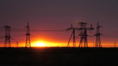 Güzel akşam güneşinin ışınlarındaki karanlık kulelerin silueti. Gün batımında yüksek voltajlı elektrik hatları. Dağıtım ve elektrik tedariği. temiz enerji