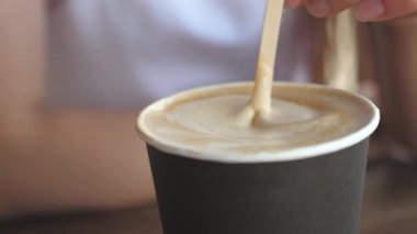 Masanın üzerinde bir bardak kahve var, bir kız lezzetli aromalı kahve karıştırıyor. Yakın plan. Kahve, sıcak bir içecek için tahta kaşığı karıştıran adam..