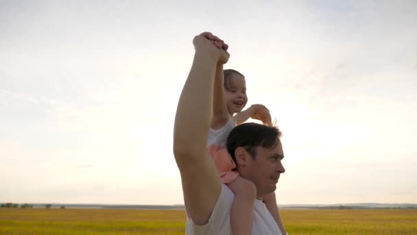 父は最愛の子供の肩を持っています,太陽の光で.父は夕日の光の中で娘と肩を並べて歩く。親のいる子供は日没時に歩く。公園で休んでる幸せな家族. — ストック動画