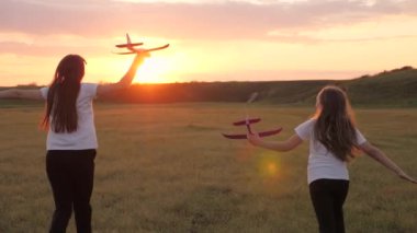Güneşin arka planındaki çocuklar ellerinde bir uçakla. Uçakta oynayan çocukların silueti. Uçma hayalleri. Mutlu çocukluk kavramı. İki kız gün batımında oyuncak bir uçakla oynuyorlar..