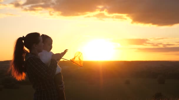 Mamá y su hija juegan tomando el sol, jugando con los rayos. concepto de una familia feliz y una infancia saludable. Mamá y el bebé lindo abrazo en el sol. Familia feliz, mamá e hija en el campo al atardecer. — Vídeo de stock