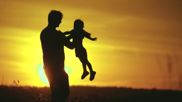 Tatínek krouží kolem své milované dcery v paprscích slunce. Šťastnou rodinu, tátu a dceru na poli při západu slunce. Otec a malá dcera si spolu hrají. Šťastná rodina a zdravé dětství koncept — Stock video