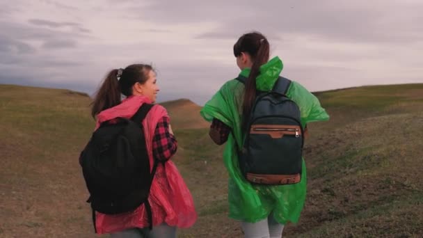 Ragazze turistiche sane viaggiano con zaini in impermeabili colorati, la tempesta si sta avvicinando. donne libere viaggiatrici vanno alla gola. viaggiatori di lavoro di squadra. Il concetto di avventura e di viaggio. — Video Stock