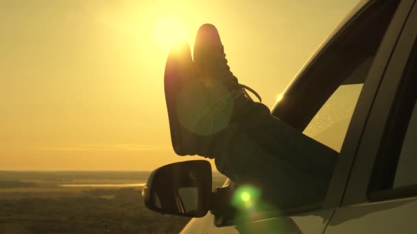 Chica libre descansando en el coche y admirando la hermosa puesta de sol de la montaña. A una joven le encanta viajar en coche, sacando las piernas por la ventana abierta y admirar el amanecer. Viajeros gratuitos, turistas. — Vídeos de Stock