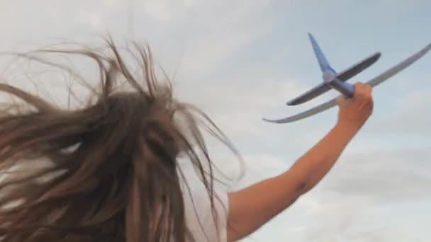 Fata vrea să devină pilot și astronaut. Mişcare lentă. Fata fericită fuge cu un avion de jucărie pe un câmp în lumina apusului de soare. Copiii joacă cu avionul de jucărie. Adolescentul visează să zboare și să devină pilot . — Videoclip de stoc