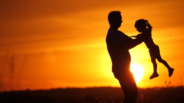 Baba ve küçük kızı birlikte oynuyorlar. Baba, sevgili kızının etrafında güneş ışınlarıyla dönüyor. Mutlu aile, gün batımında bir tarlada baba ve kız. Mutlu aile ve sağlıklı çocukluk kavramı — Stok video