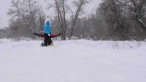 Família feliz jogando no inverno no Parque para férias de Natal. Mãe e filha engraçadas montam o pai num trenó na neve. os pais se divertem com seu filho na floresta na neve. ano novo — Vídeo de Stock