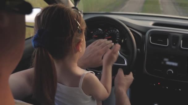 Papai ensina sua filhinha a girar o volante enquanto está sentado em seu carro no assento dos motoristas. pai viaja com crianças de carro. O condutor e o miúdo estão a conduzir. família feliz e conceito de infância — Vídeo de Stock