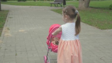 Küçük kız elinde bebek arabası ve oyuncak ayıyla parkta yürüyor. Sokakta en sevdiği oyuncağıyla dolaşan bir çocuk. Çocuk oyun parkında oynuyor. sağlıklı çocukluk kavramı