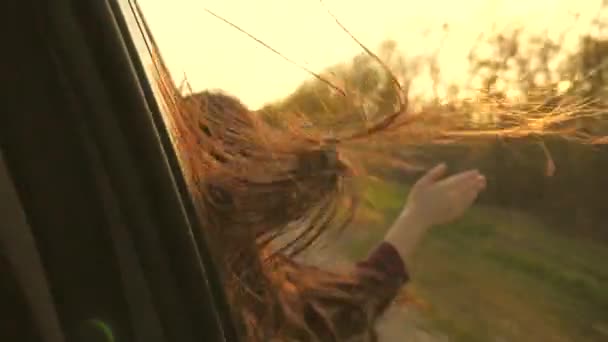 Meisje reiziger met lang haar reist, zit op de voorbank van de auto, steekt zijn hand uit het raam en vangt schittering van de zon. Vrije vrouw rijdt auto, vangt wind met haar hand uit het autoraam. reizen en — Stockvideo