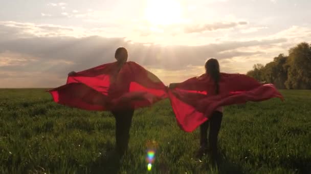 Anak-anak berjas hujan merah memerankan pahlawan super yang berlari di padang rumput hijau. Permainan anak-anak dan mimpi. Gerakan lambat. Impian remaja untuk menjadi superhero. gadis muda berjubah merah — Stok Video