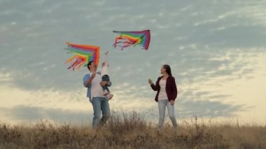 Baba ve çocuklar parkta uçurtmalarla oynuyorlar. Küçük kız neşeyle uçurtmayı eliyle yakalıyor. Açık hava aile oyunu. Baba ve sağlıklı kızlar renkli kağıt uçakları gökyüzüne fırlattılar.