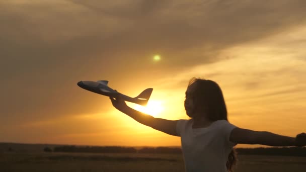 Chica quiere convertirse en piloto y astronauta. En cámara lenta. Chica feliz corre con un avión de juguete en un campo en la luz del atardecer. niños juegan juguete avión. adolescentes sueña con volar y convertirse en piloto. — Vídeos de Stock