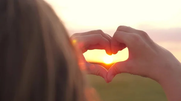 The girl made a beautiful heart from her finger in the rays of the sun. healthy woman making heart shape with hands at sunset. Shining summer sun on your hands. healthy heart concept.