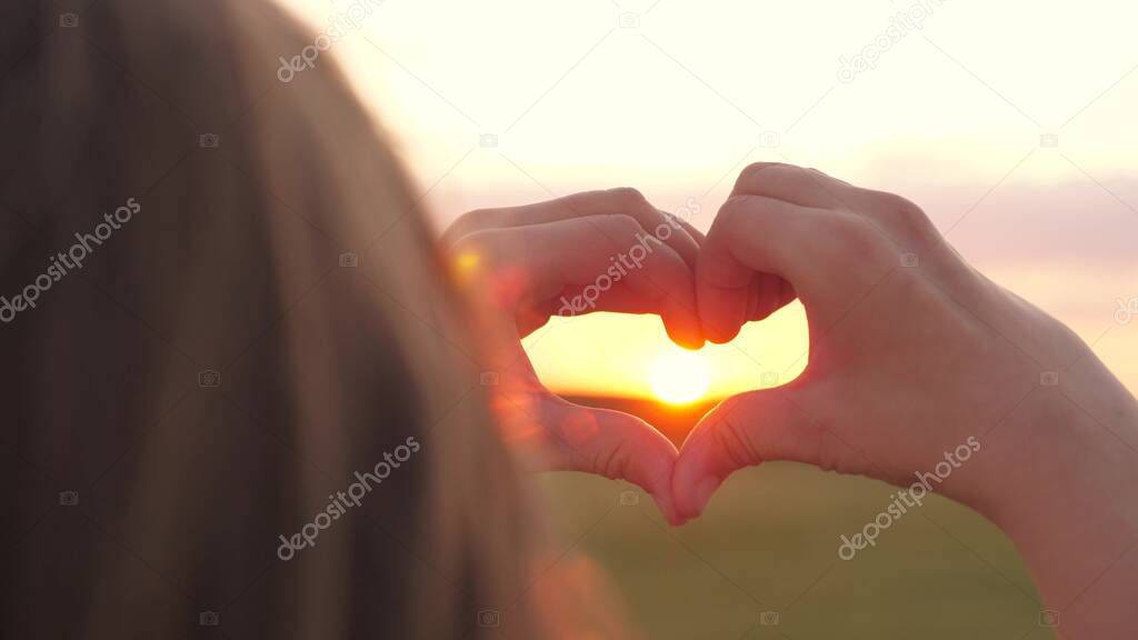 The girl made a beautiful heart from her finger in the rays of the sun. healthy woman making heart shape with hands at sunset. Shining summer sun on your hands. healthy heart concept.