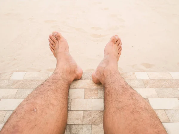 Rahatlatıcı bir adamdır sahilde yalınayak. Asya adamın cilt ve erkekler kıllı bacakları kum zemin üzerine closeup bacaklar. Adamın bacakları kum üzerinde.