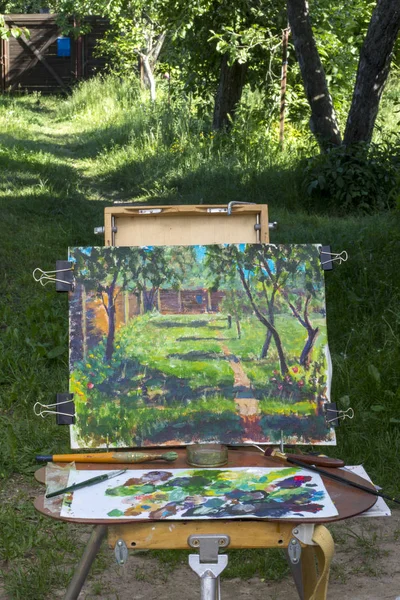 Plein air in sunny landscape nature. Canvas on sketchpad, a palette with used paints. Drawing in yard.