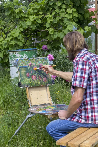 male artist paint on plein air flowers pink peonies painting on nature. Plein air painting of beautiful peony flowers bush