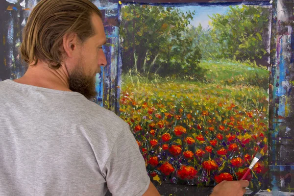 Bearded man painter artist paints with brush a red poppies flowers in forest landscape painting on canvas. In artist\'s studio, art education, creative, creativity.