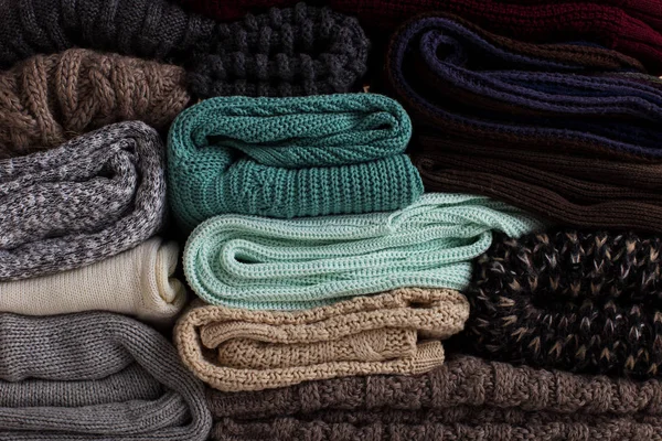 A stack of knitted clothes of different colors and textures.