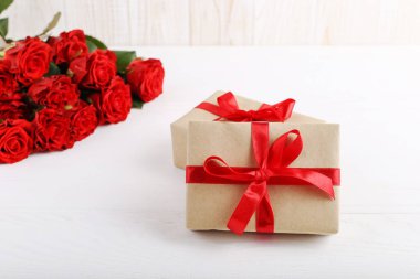 Bir buket kırmızı gül, beyaz tahta masada bir hediye. Konsept Kadınlar Günü veya St Valentine. Kopyalama alanı.