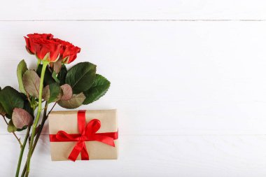 Bir buket kırmızı gül, beyaz tahta masada bir hediye. Konsept Kadınlar Günü veya St Valentine. Kopyalama alanı.