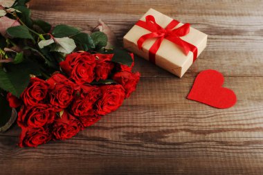 Tahta masaüzerinde kırmızı güller, hediye ve kalplerden oluşan bir buket. Konsept Kadınlar Günü veya St Valentine. Kopyalama alanı.