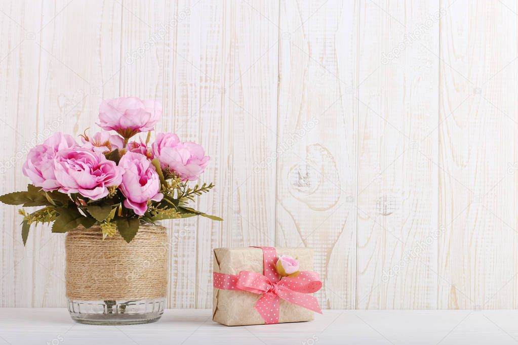 Pink flowers in vase and gift in craft paper on the table. Concept of Women's Day or St. Valentine.