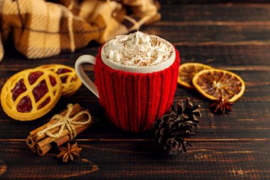 Bir bardak krem şanti ve toz, örme bir kapak ve ev yapımı kurabiye, Cezve ve baharatlar, sıcak içecek damalı halı yakınındaki ahşap bir masa üzerinde yalan. Kopya alanı.