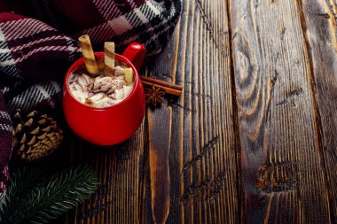 Kış kahvesi, kremalı kakao ve kırmızı seramik fincanda marşmelov. Tahta bir masanın üzerinde, kareli bir eşarbın yanında. Metin için yer, kopyalama alanı.
