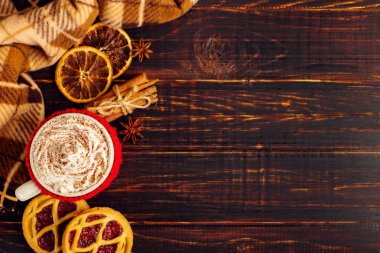 Bir bardak krem şanti ve toz, örme bir kapak ve ev yapımı kurabiye, Cezve ve baharatlar, sıcak içecek damalı halı yakınındaki ahşap bir masa üzerinde yalan. Kopya alanı.