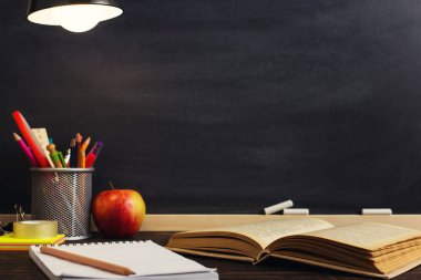 Öğretmenin masası ya da bir işçi, hangi yazı malzemeleri yalan, bir kitap ve bir elma, akşam lamba altında. Okul teması için metin veya arka plan için boş. Kopyalama alanı.