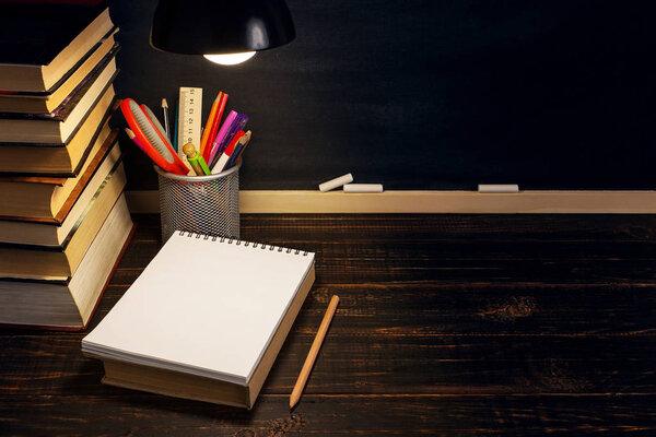 The teacher's desk or a worker, on which the writing materials lie, a books, in the evening under the lamp. Blank for text or background for a school theme. Copy space.