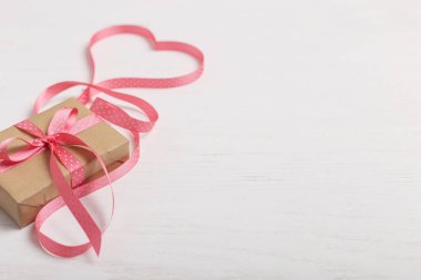 Kraft kağıt ve pembe bir kurdele Beyaz ahşap bir masa üzerinde bir hediye. Metin, kopya alanı, Sevgililer günü kartpostal için yer.