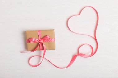 Kraft kağıt ve pembe bir kurdele Beyaz ahşap bir masa üzerinde bir hediye. Metin, kopya alanı, Sevgililer günü kartpostal için yer.