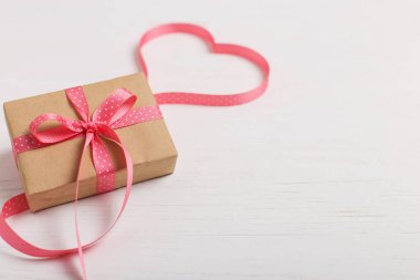 Kraft kağıt ve pembe bir kurdele Beyaz ahşap bir masa üzerinde bir hediye. Metin, kopya alanı, Sevgililer günü kartpostal için yer.