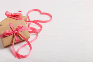 Kraft kağıt ve pembe bir kurdele Beyaz ahşap bir masa üzerinde bir hediye. Metin, kopya alanı, Sevgililer günü kartpostal için yer.