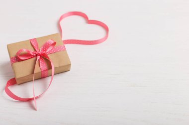 Kraft kağıt ve pembe bir kurdele Beyaz ahşap bir masa üzerinde bir hediye. Metin, kopya alanı, Sevgililer günü kartpostal için yer.