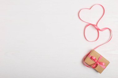 Kraft kağıt ve pembe bir kurdele Beyaz ahşap bir masa üzerinde bir hediye. Metin, kopya alanı, Sevgililer günü kartpostal için yer.